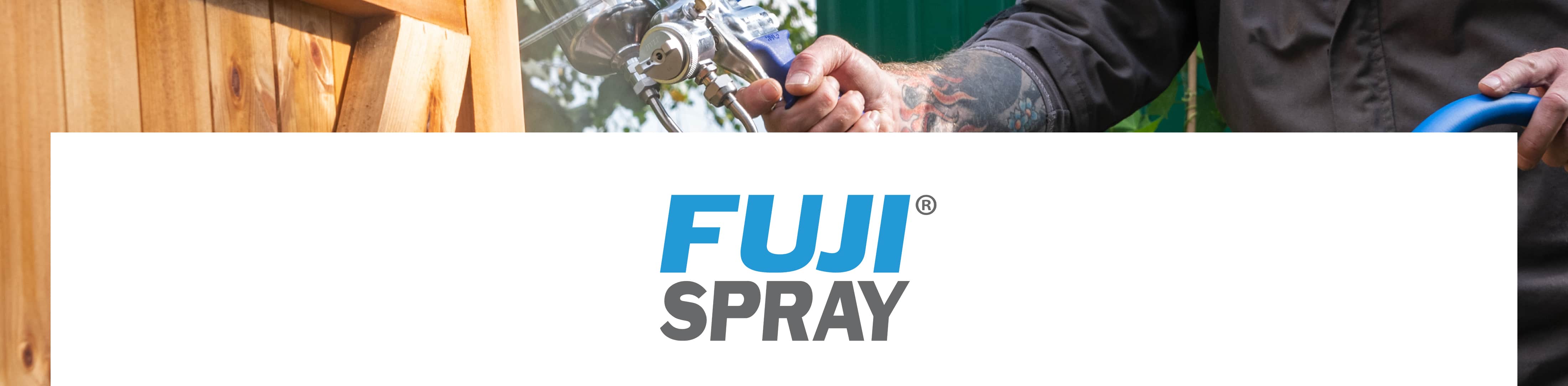 A close-up of a person holding a blue spray gun in front of a wooden fence, with a large white banner across the center featuring the blue and gray FUJI SPRAY logo.