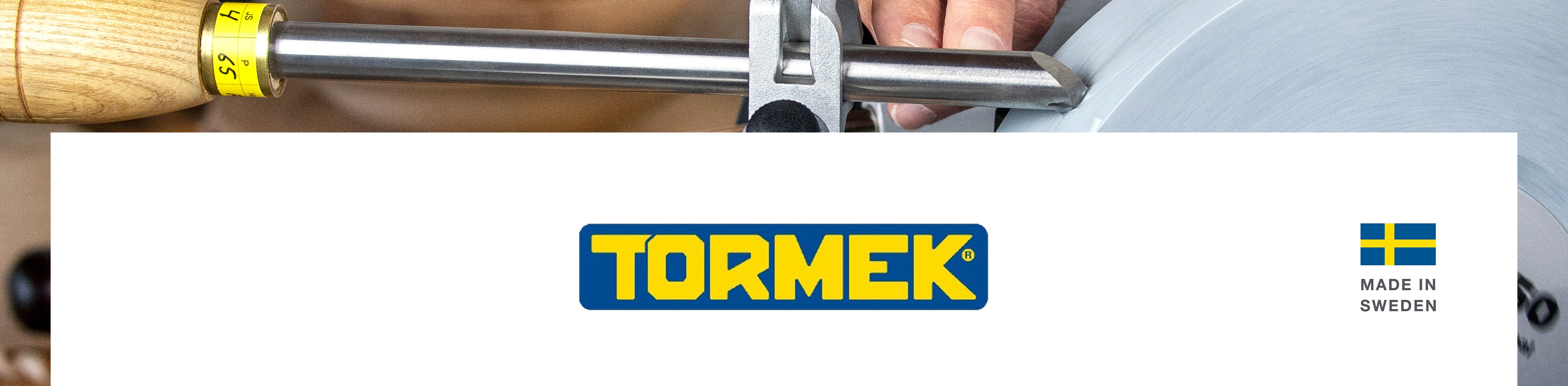 A close-up of a Tormek sharpening machine in use. A chisel is being sharpened, there is a yellow and black scale marker on the chisel, and a hand holding the tool. A white banner across the bottom features the Tormek logo and a small Swedish flag with 'Made in Sweden' text.