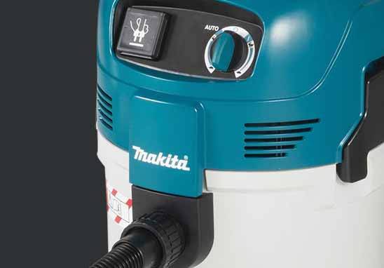 Close-up of a Makita wet/dry vacuum cleaner showing the teal and white body, control panel with switch and dial, and part of the black hose against a dark grey background.