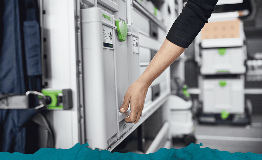 A person's hand reaching toward a white storage locker with a green handle inside a van filled with storage racks.