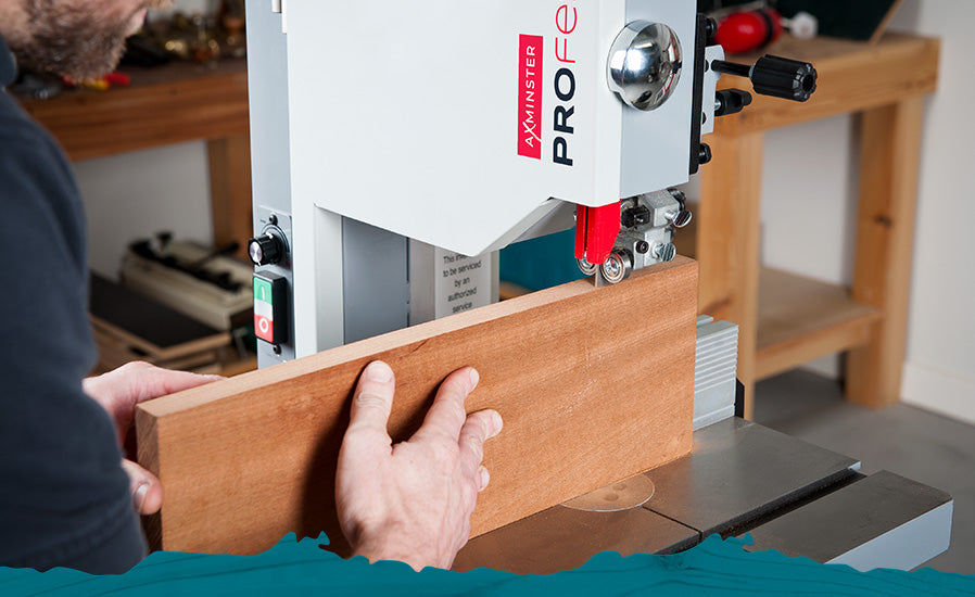 A person using an Axminster Professional bandsaw to cut a piece of wood in a workshop setting.
